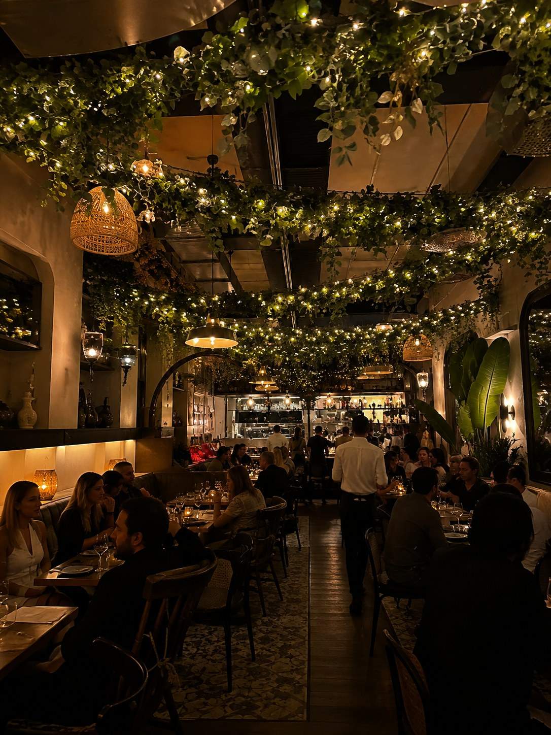 Restaurant dining room with a ceiling of hanging greenery and string lights, styled by Light the Lights