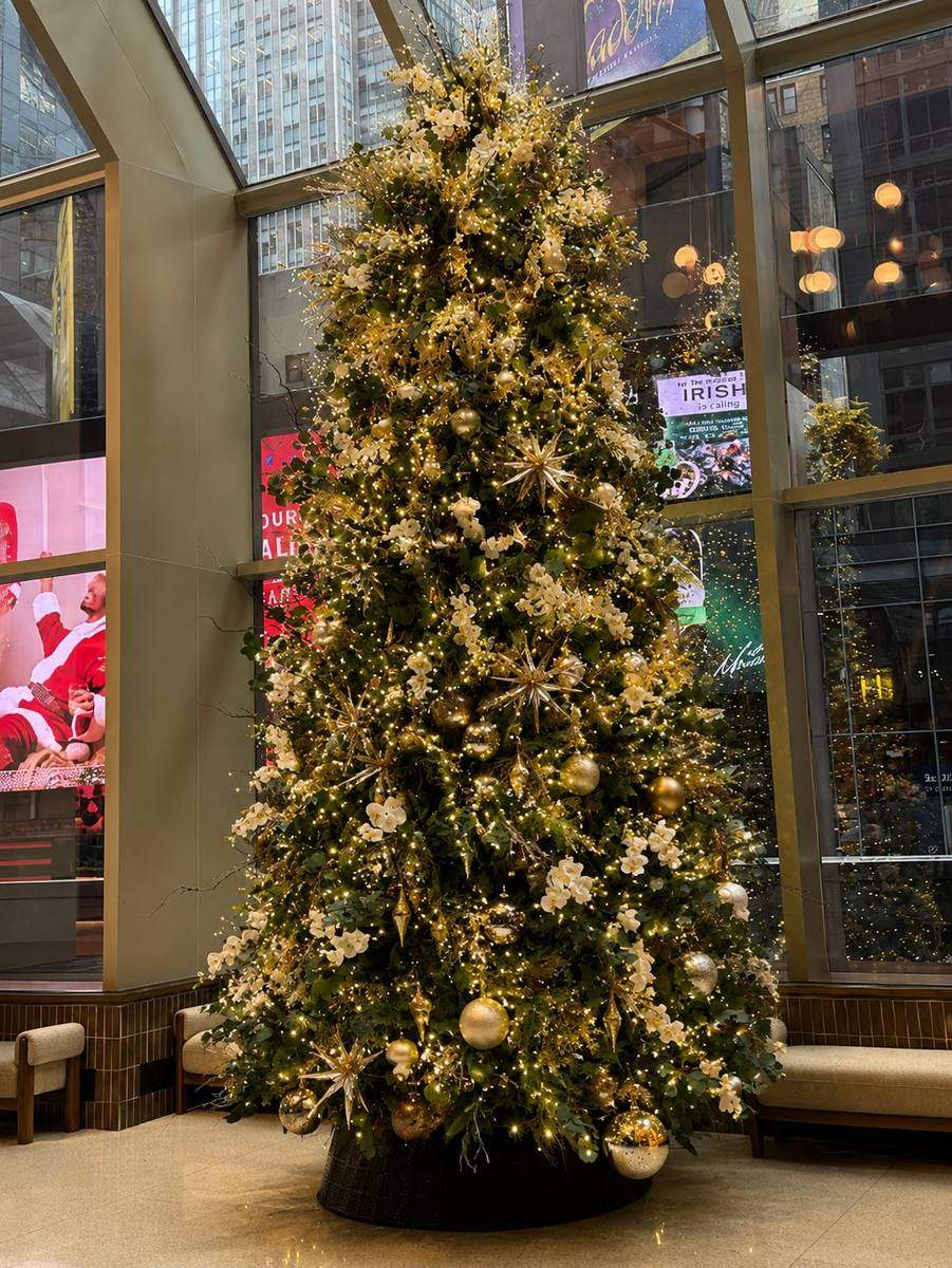 Gold and white Christmas tree in a lobby with floor-to-ceiling city view windows, styled by Light the Lights