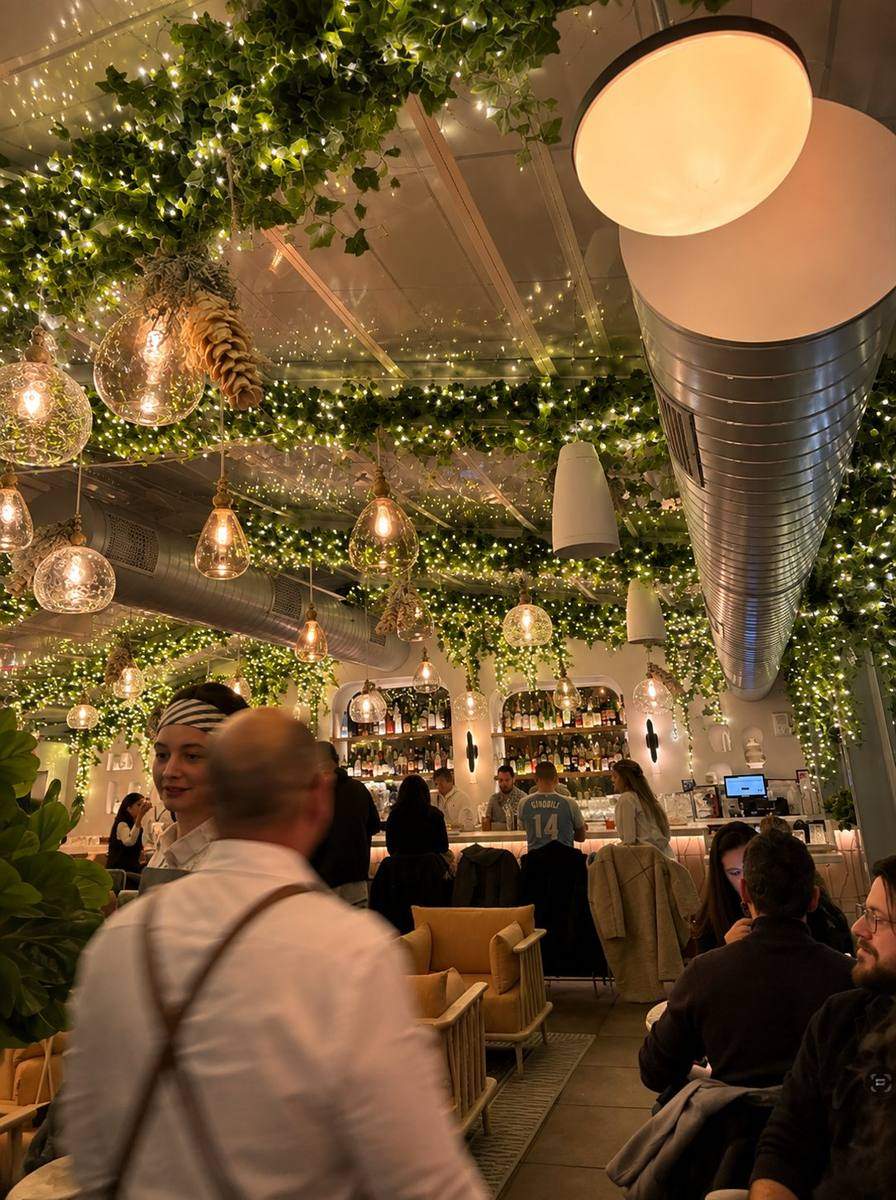 Restaurant ceiling wrapped in hanging greenery and string lights over the bar, styled by Light the Lights