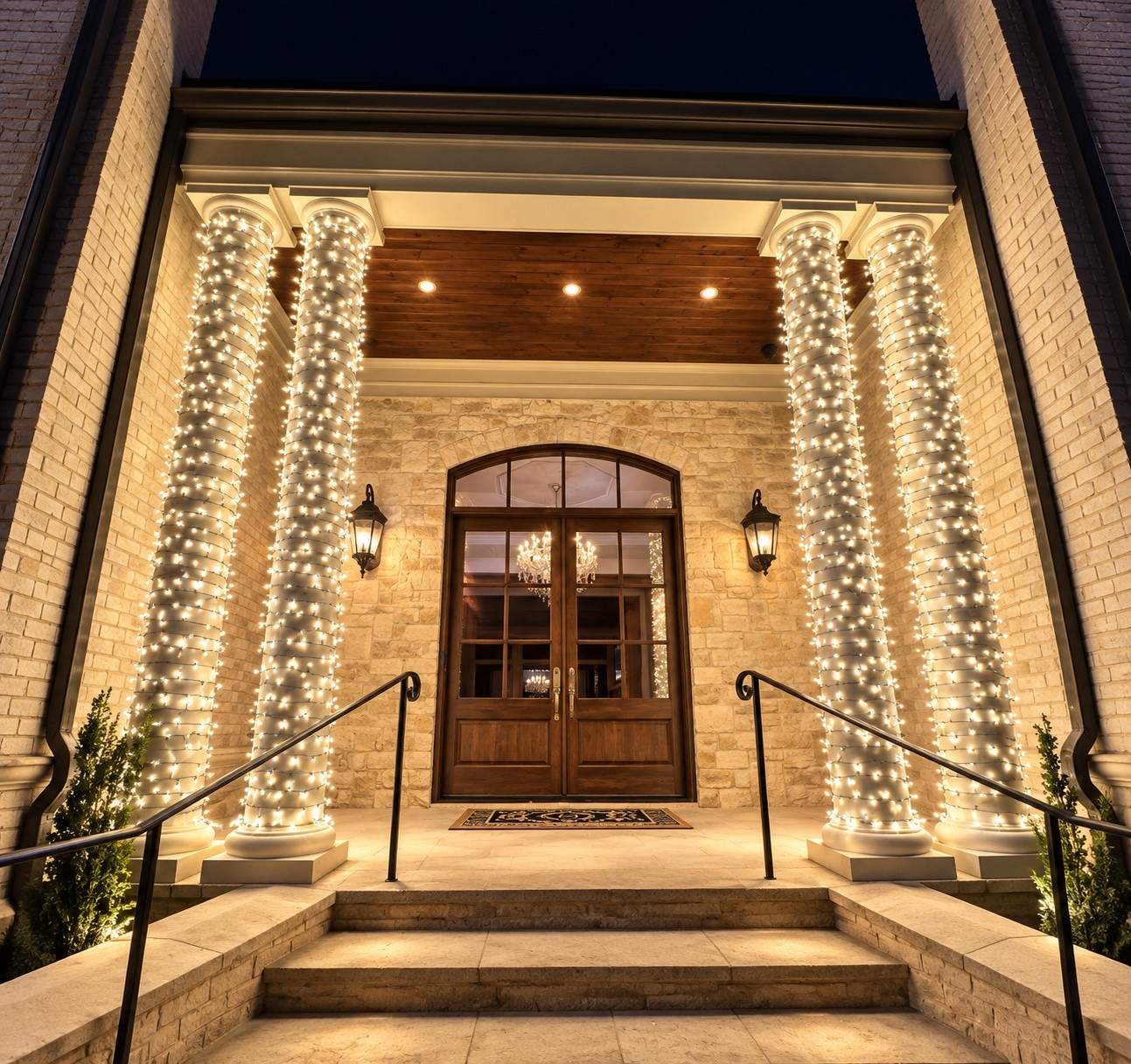 Four stone entry columns wrapped in warm white lights at a home entrance